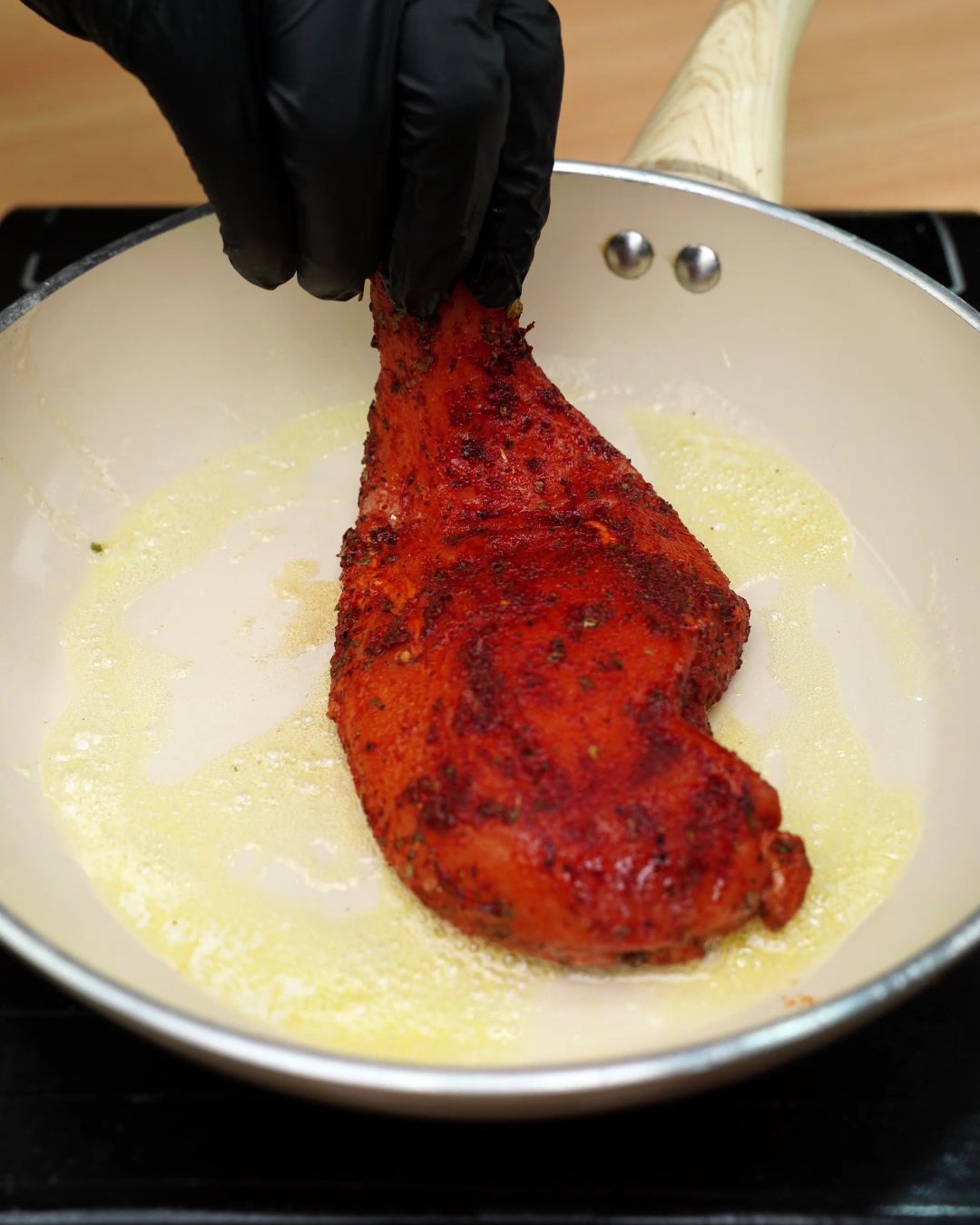 A paprika-coated chicken breast being laid into melted butter in a skillet