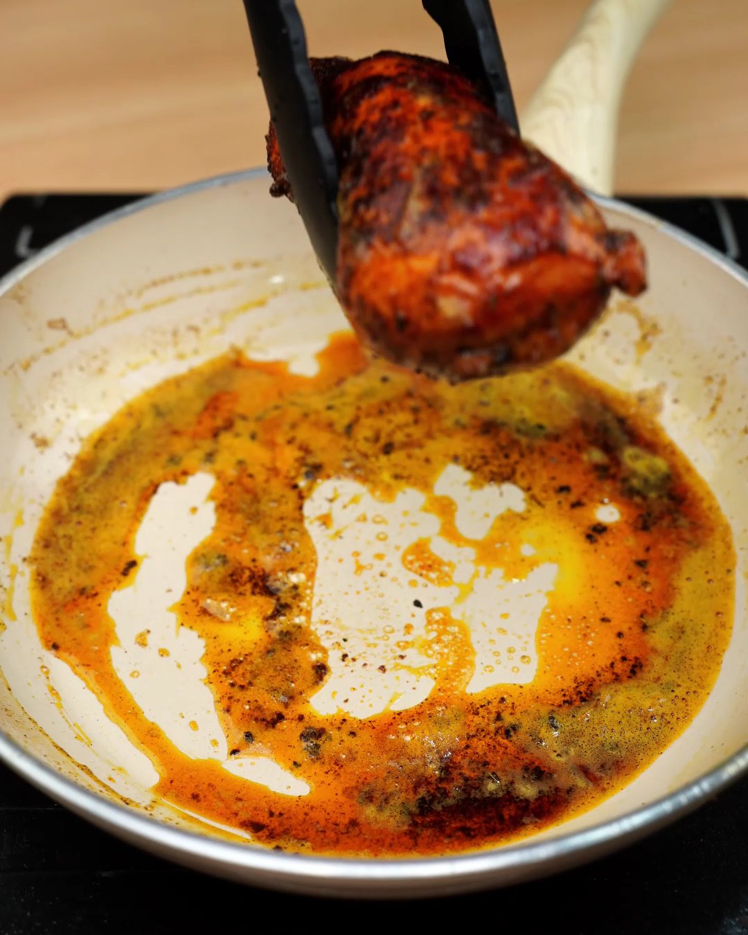 A seared paprika chicken breast being lifted from the skillet with tongs