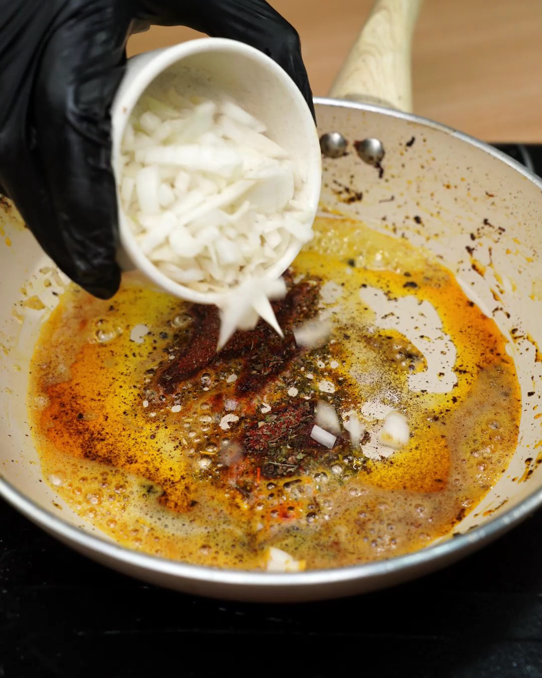 Diced onion being added to the spiced butter in a skillet