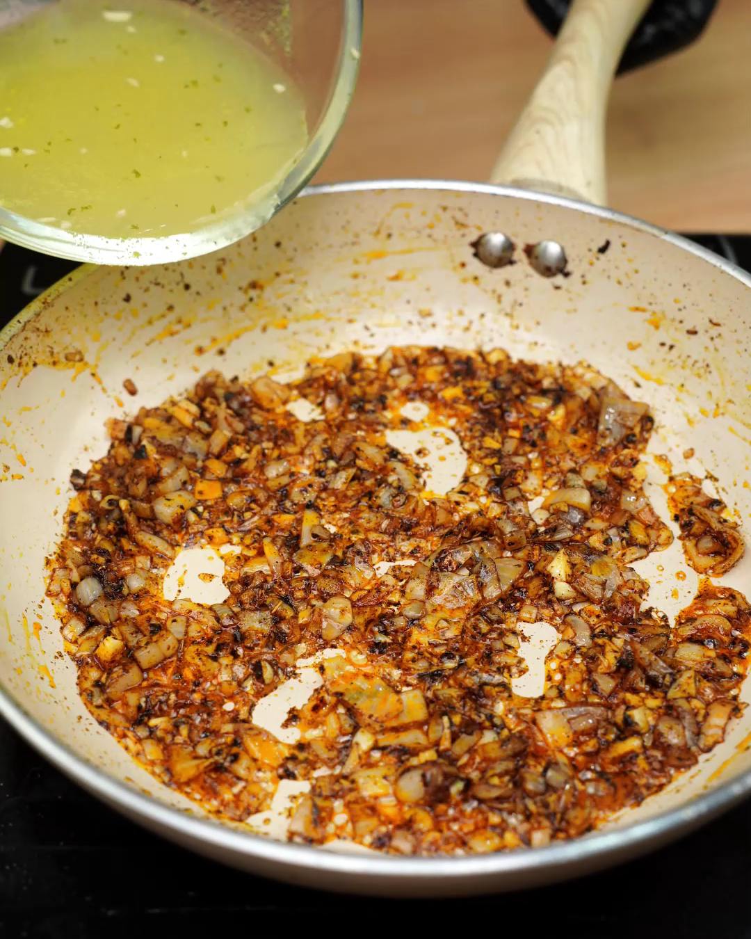 Golden broth being poured into the onion and garlic mixture