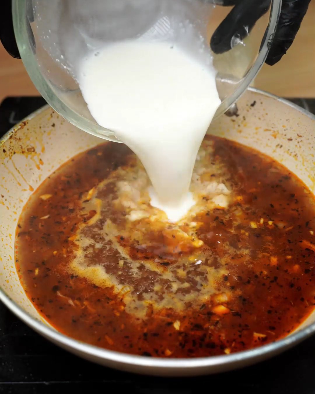 Heavy cream being poured into the spiced broth in a skillet