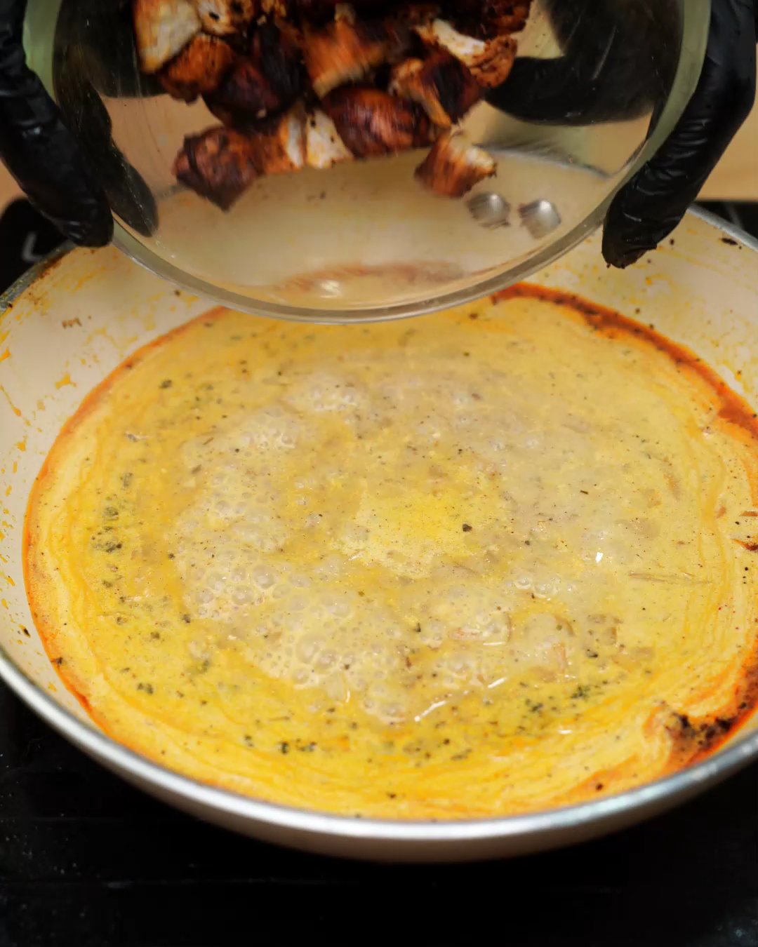 Pieces of seared paprika chicken being added to the creamy sauce
