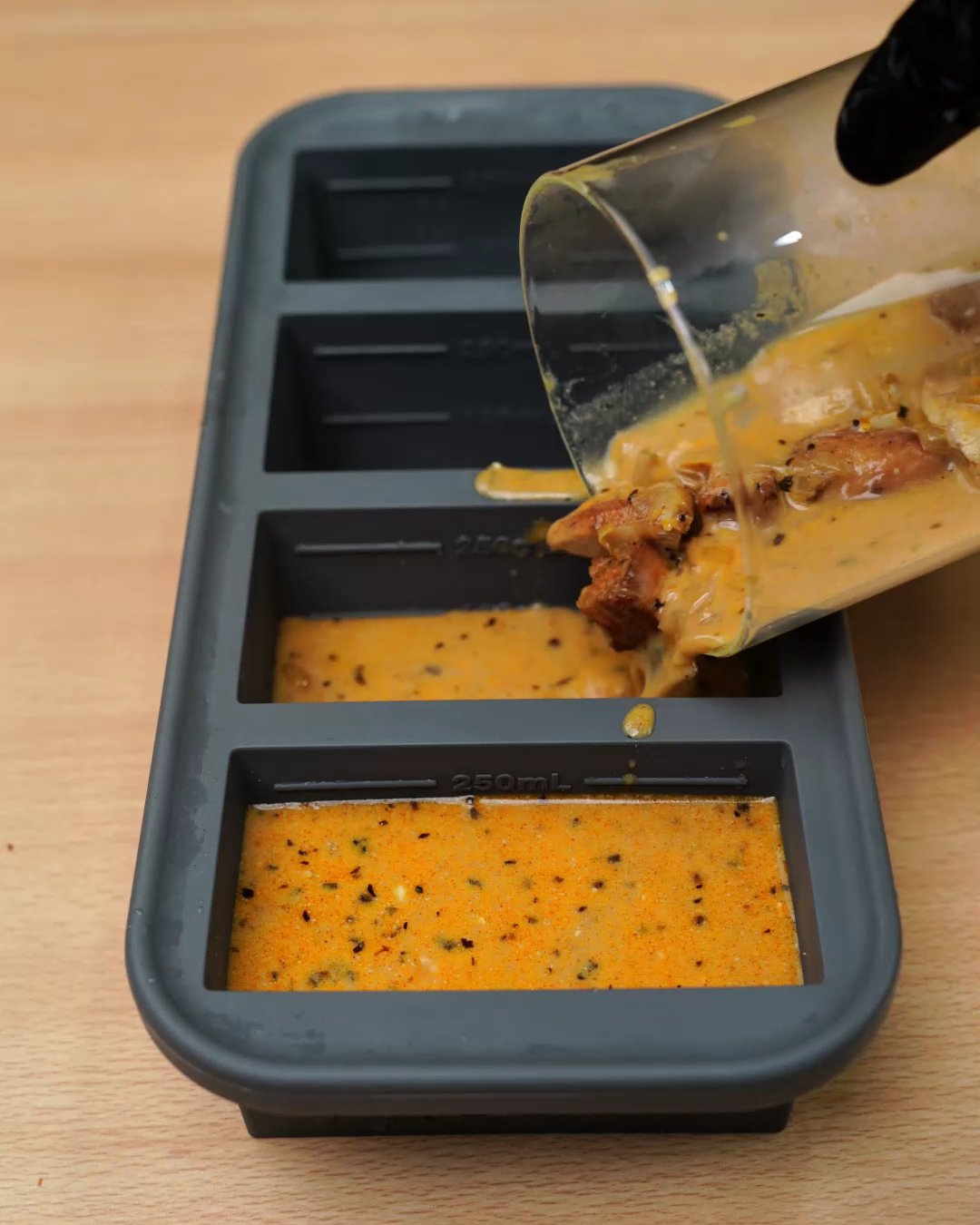 Creamy paprika chicken sauce being poured into a gray silicone freezer mold