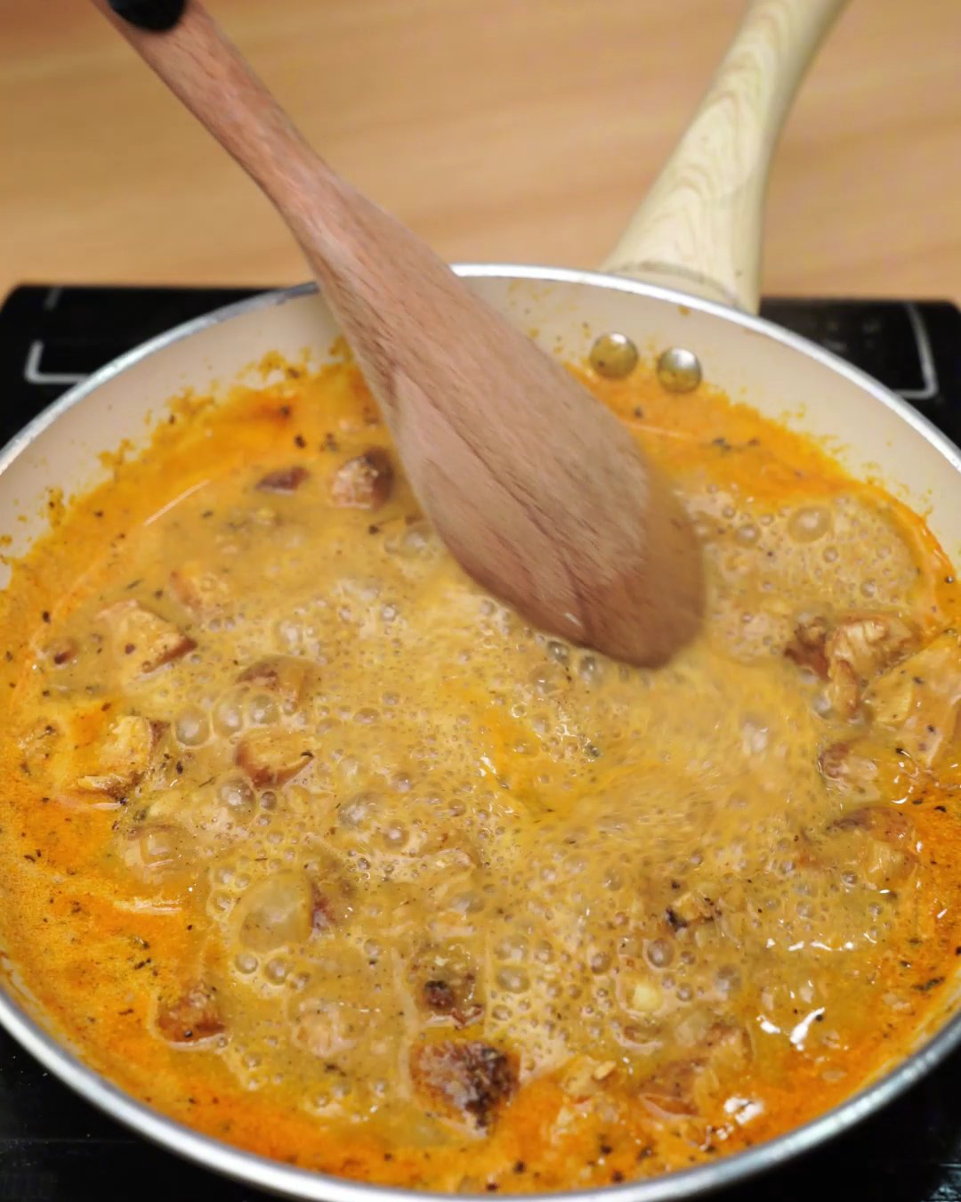 Melted creamy paprika chicken sauce being stirred with a wooden spoon