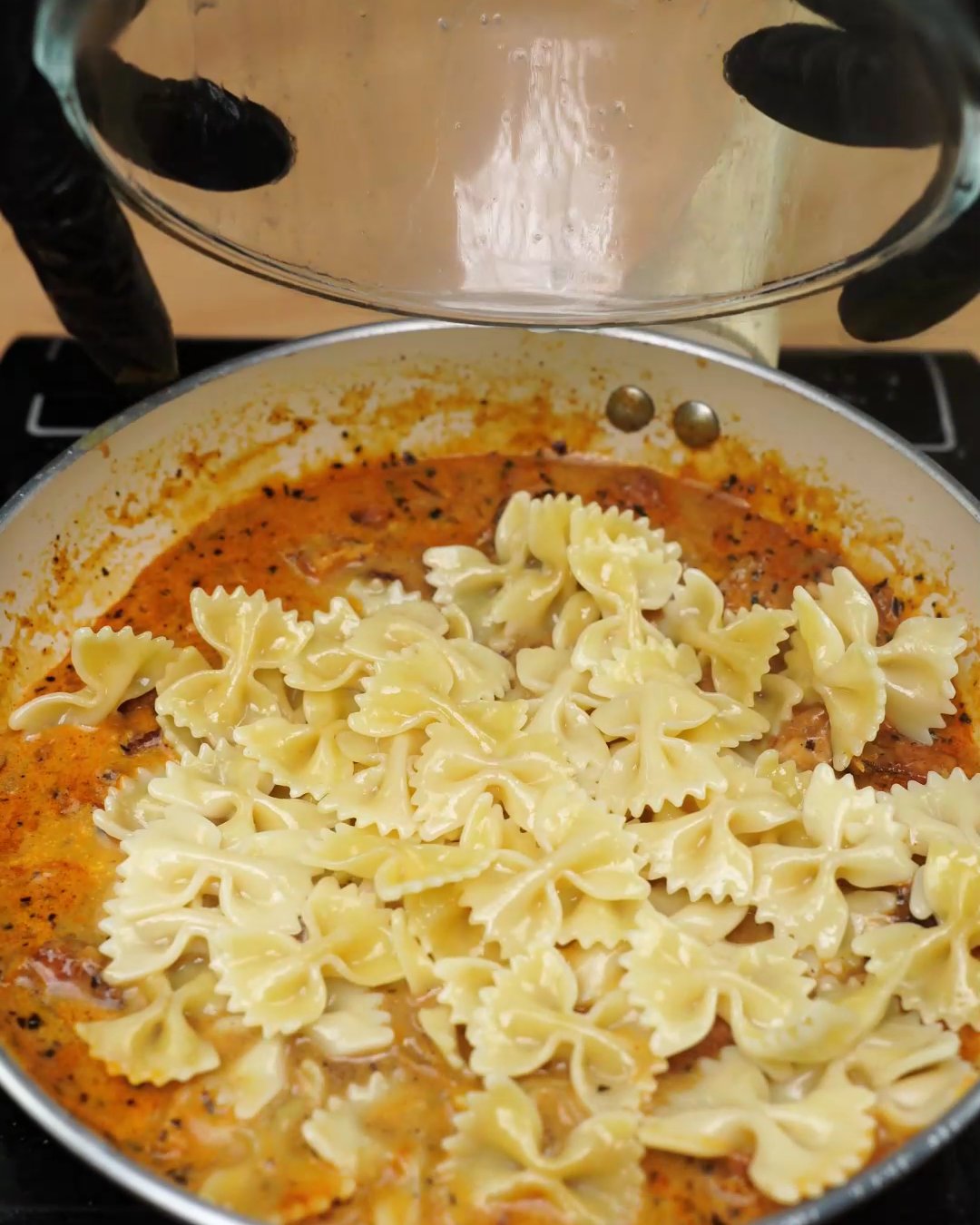 Cooked bowtie pasta added on top of the creamy paprika chicken sauce