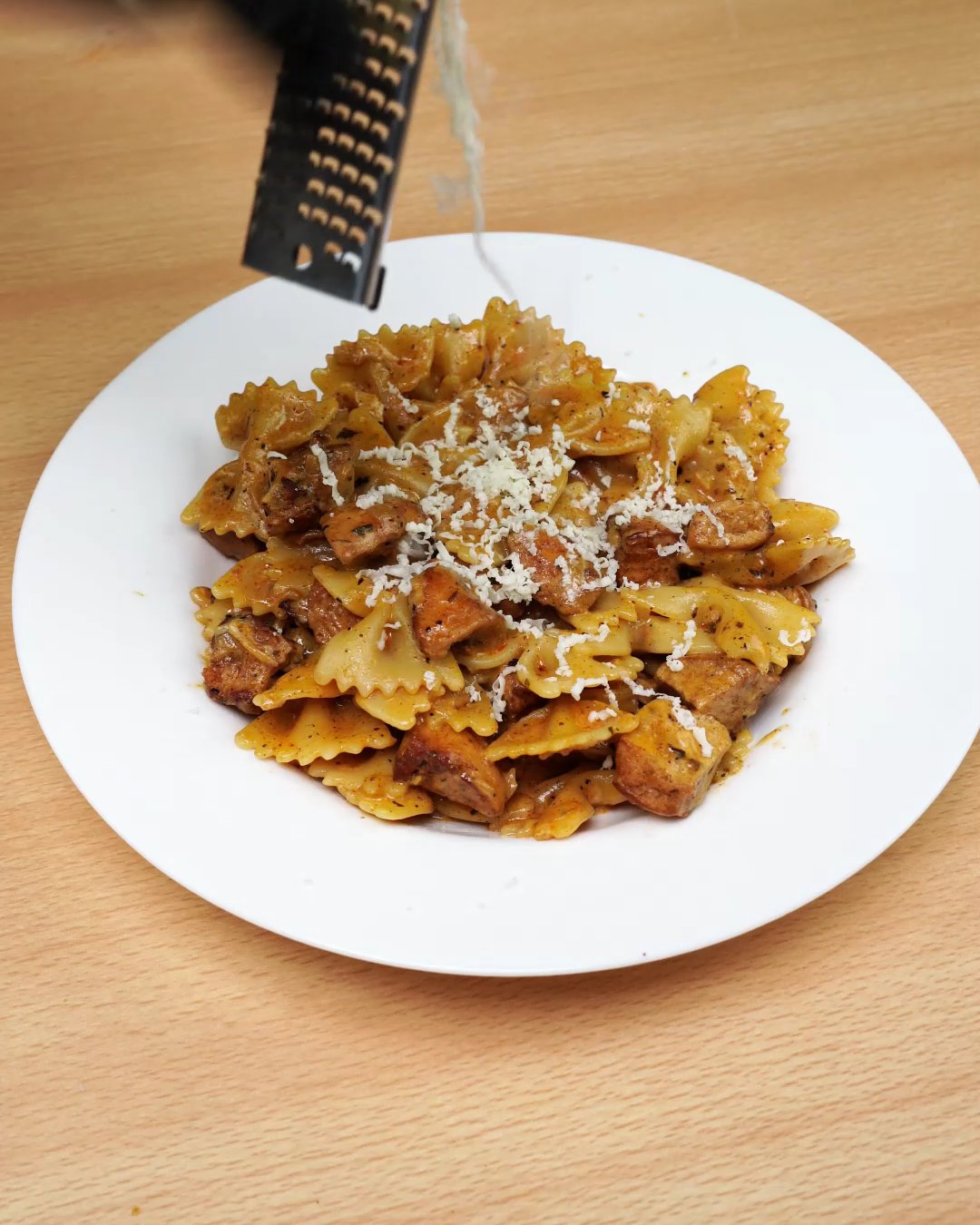 Parmesan being grated over a plate of creamy paprika chicken bowtie pasta