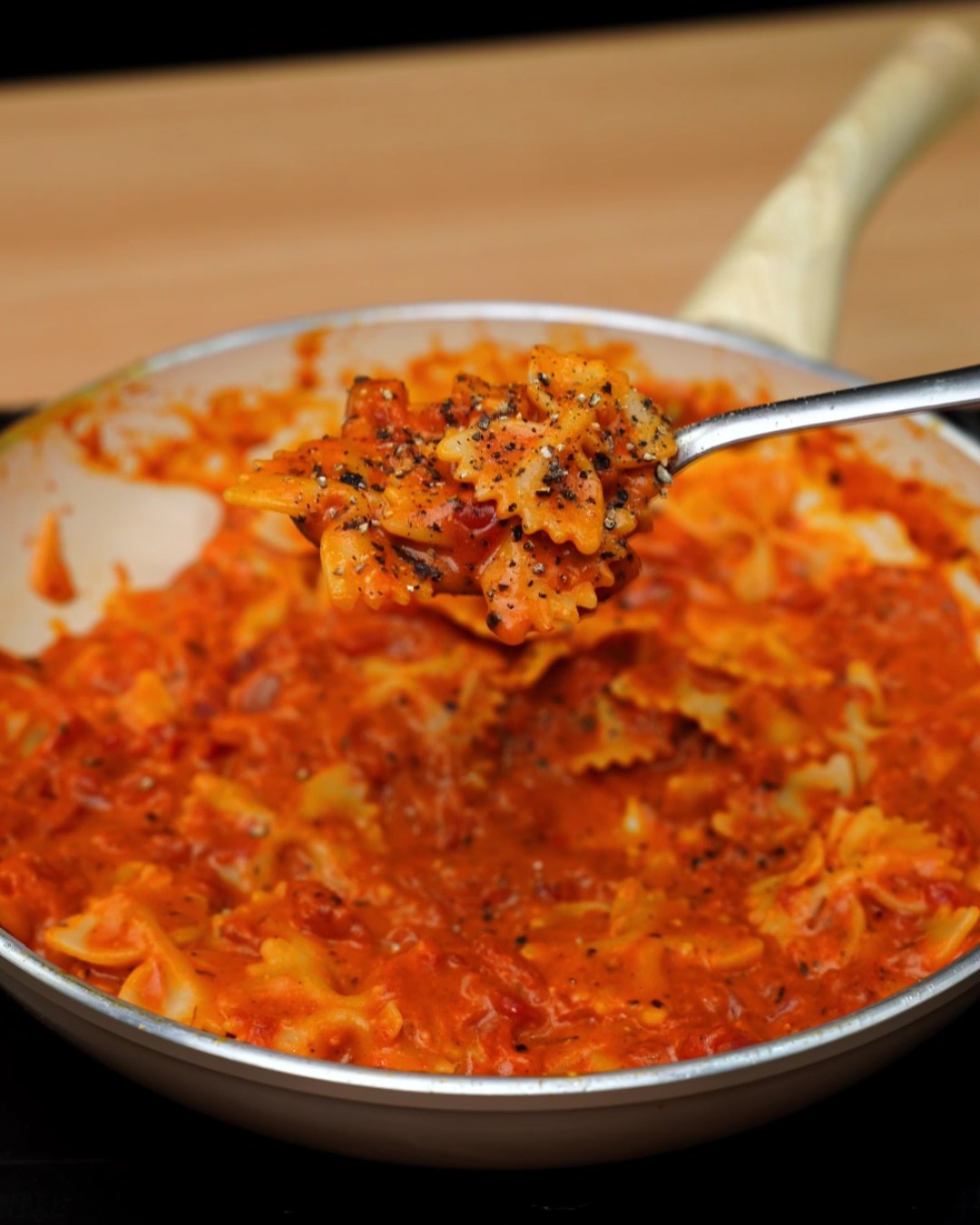 Creamy tomato bowtie pasta on a spoon, topped with cracked black pepper