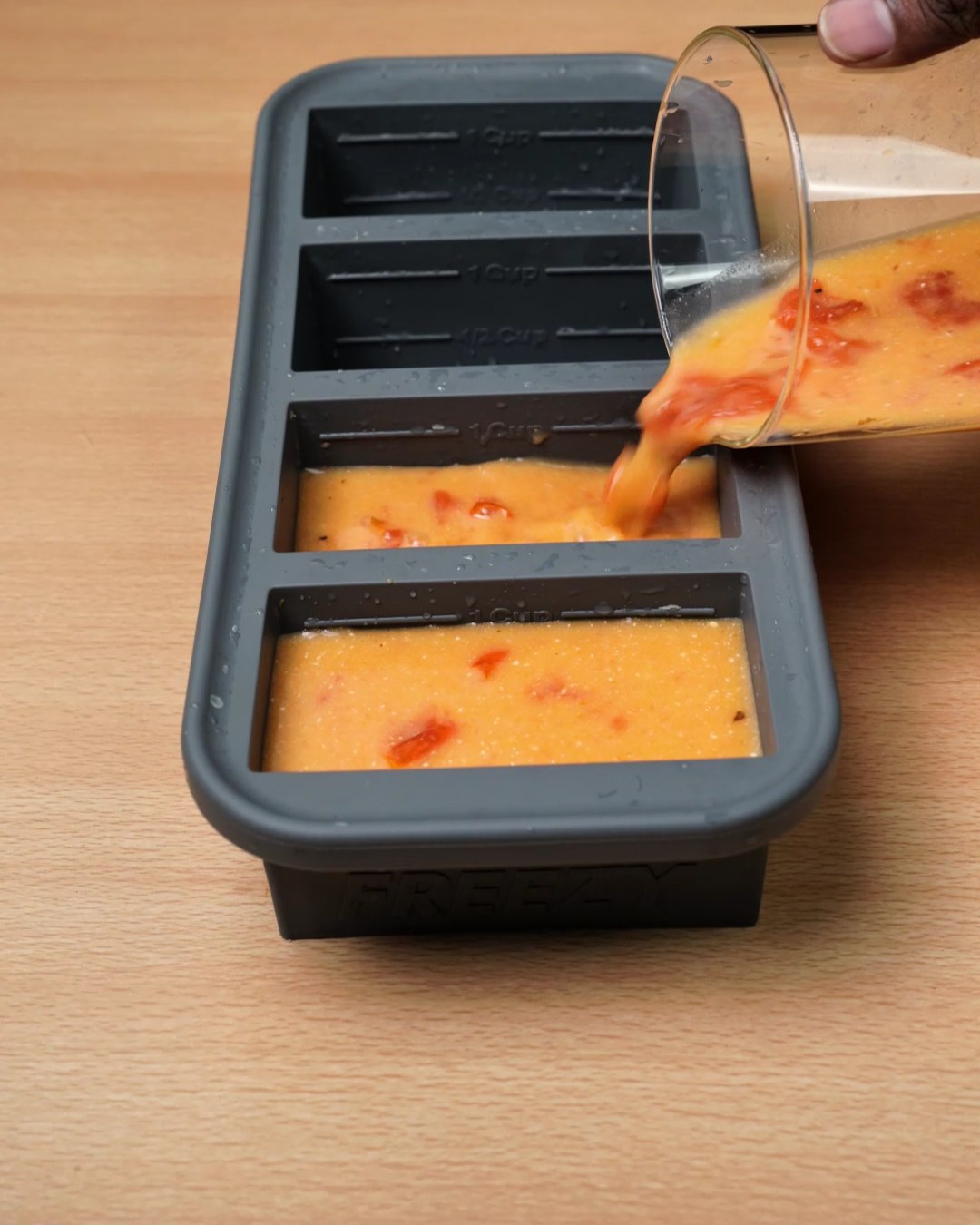 Pouring creamy tomato sauce into a silicone freezer mold
