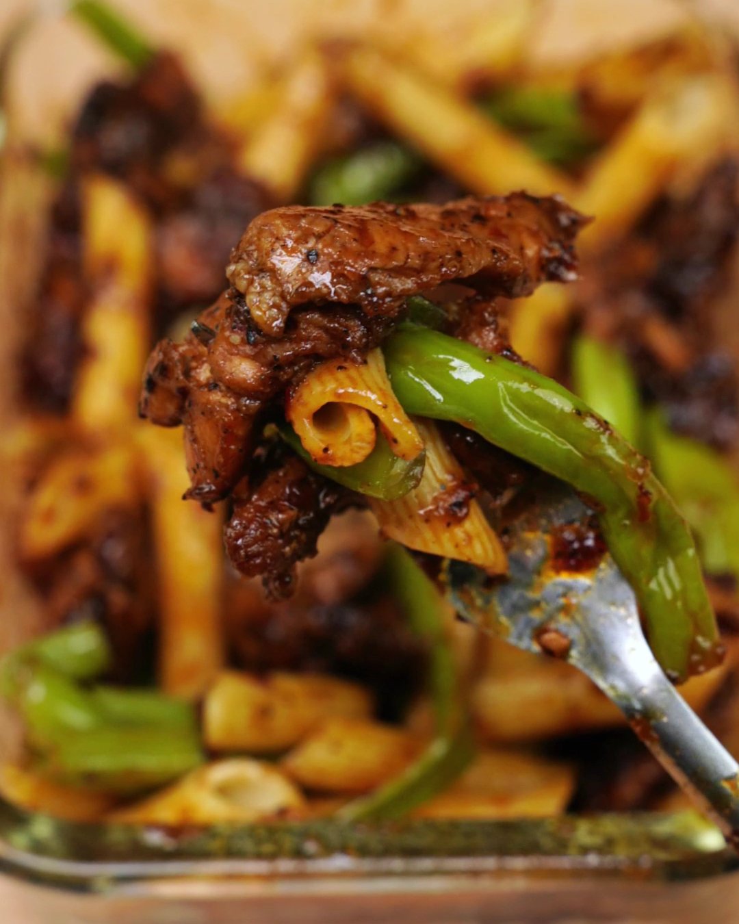 Close-up of a forkful of honey chicken, penne and green beans held over a glass meal prep container