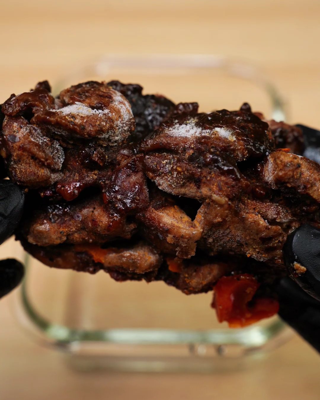Gloved hand holding a frozen block of glazed honey chicken pieces over a glass container