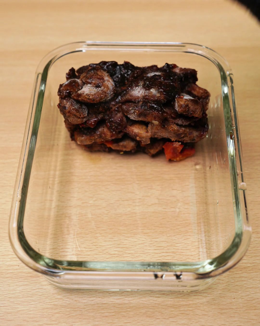 Frozen block of honey chicken placed at one end of an empty glass meal prep container