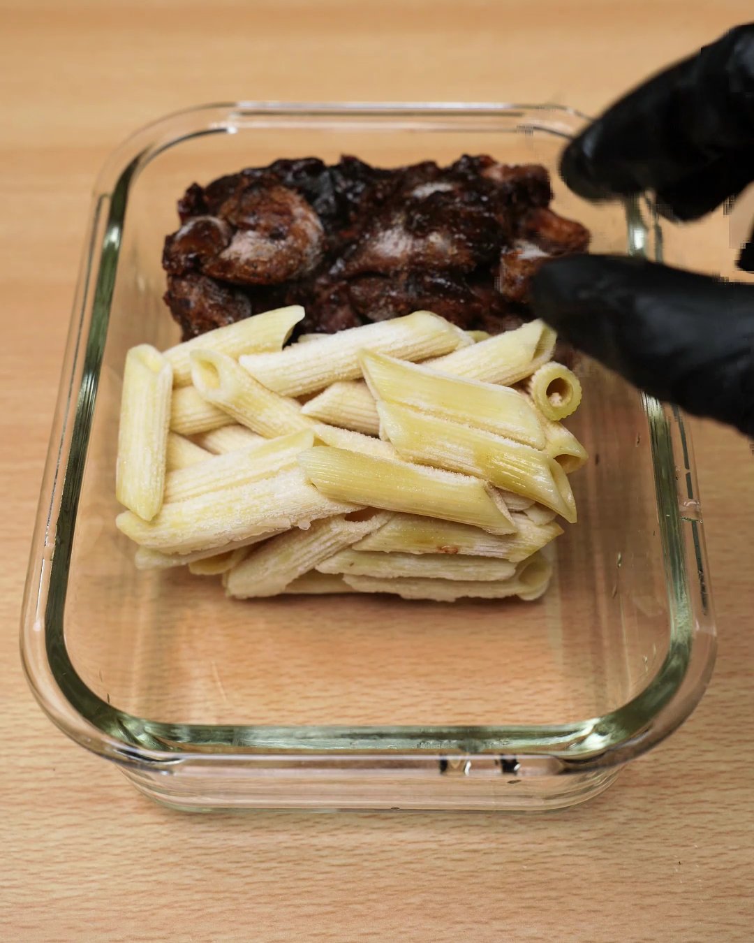 Frozen block of penne being placed next to the frozen honey chicken in a glass container