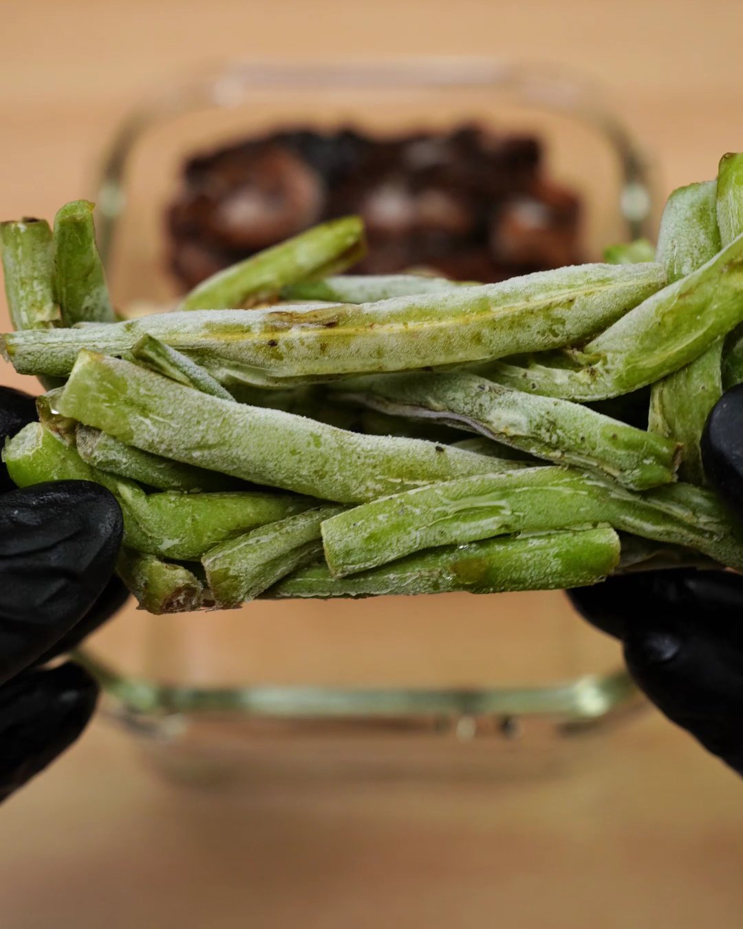 Frozen block of green beans held above a glass container with frozen chicken and penne
