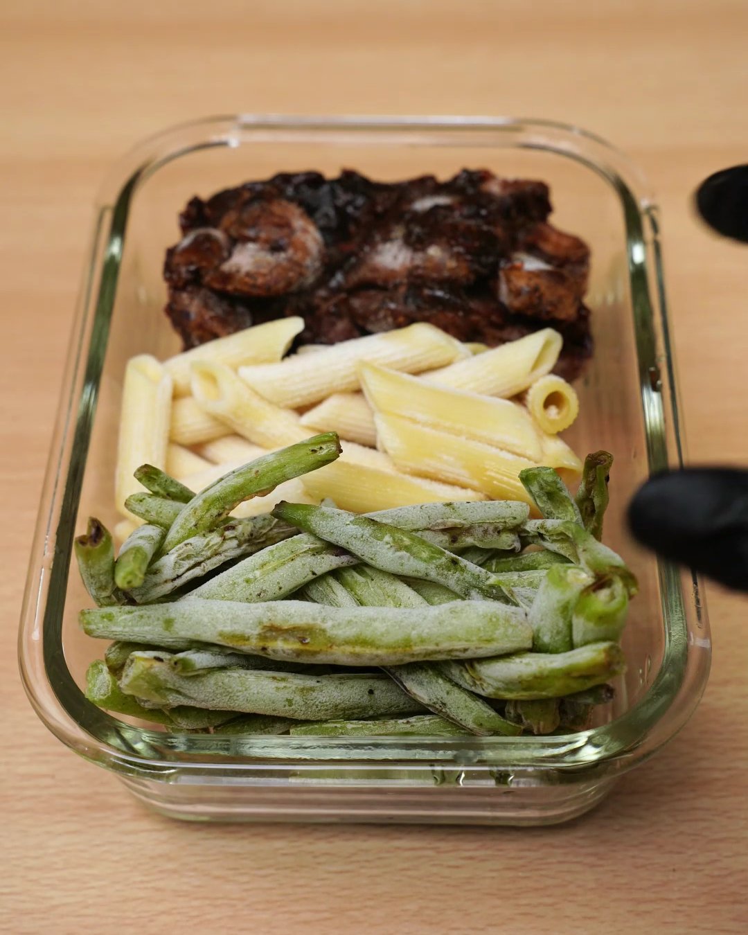 Glass container with frozen blocks of honey chicken, penne and green beans side by side