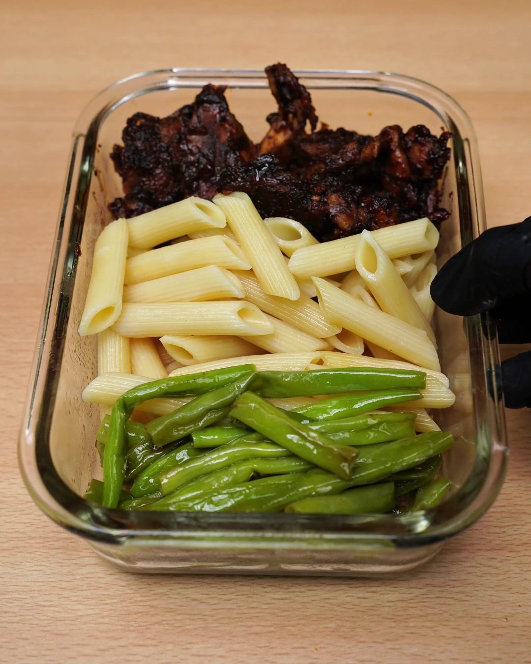 Reheated honey chicken, penne and bright green beans side by side in a glass container