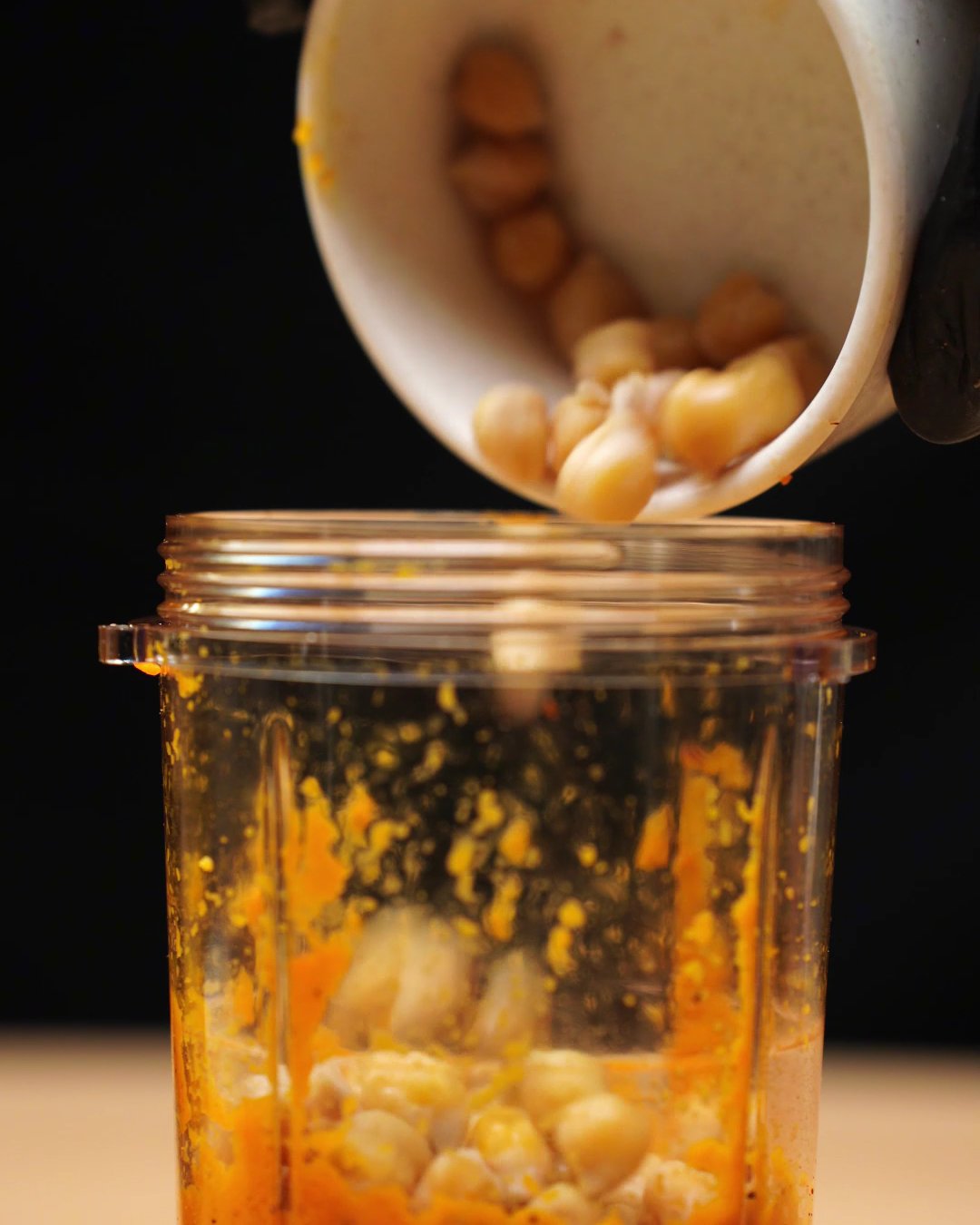 Chickpeas being poured from a bowl into the blended carrot puree