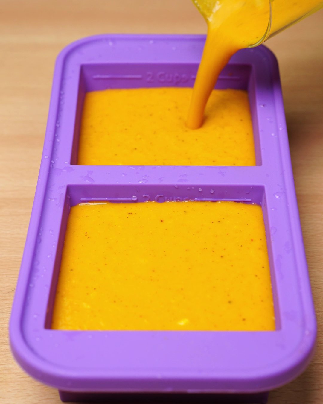 Carrot soup being poured into a purple silicone freezer mold
