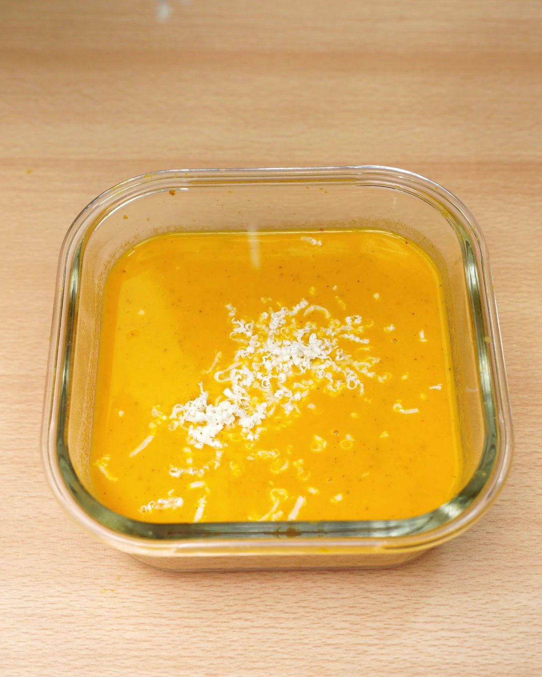 Grated Parmesan sprinkled over hot carrot soup in a glass dish