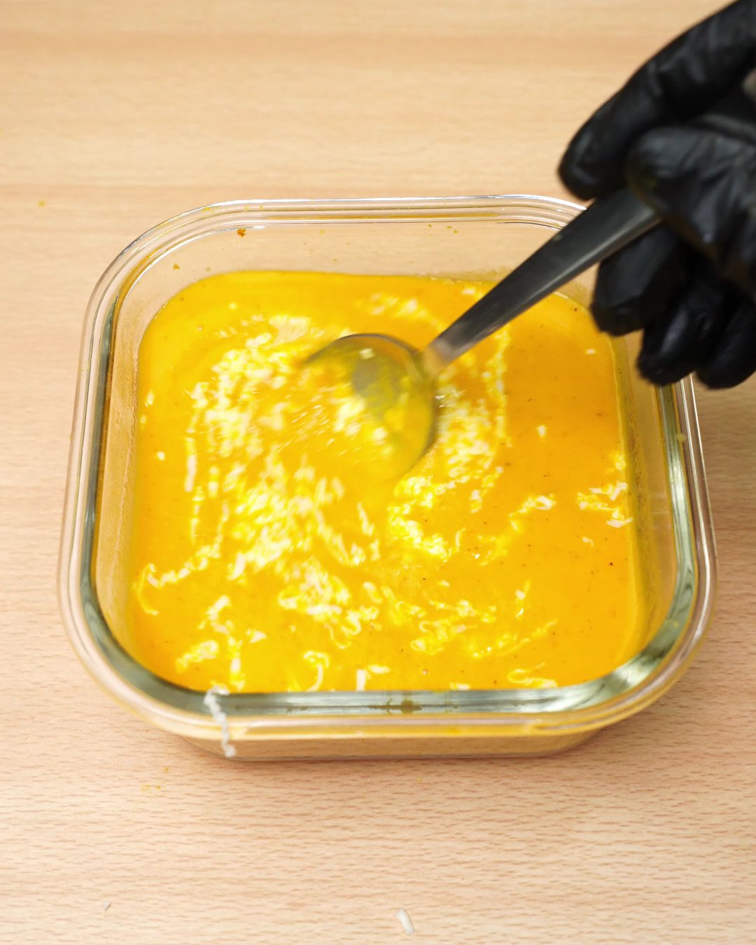 Grated Parmesan being stirred into carrot soup with a spoon