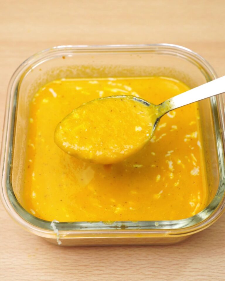 A spoonful of creamy roasted carrot and chickpea soup over a glass dish