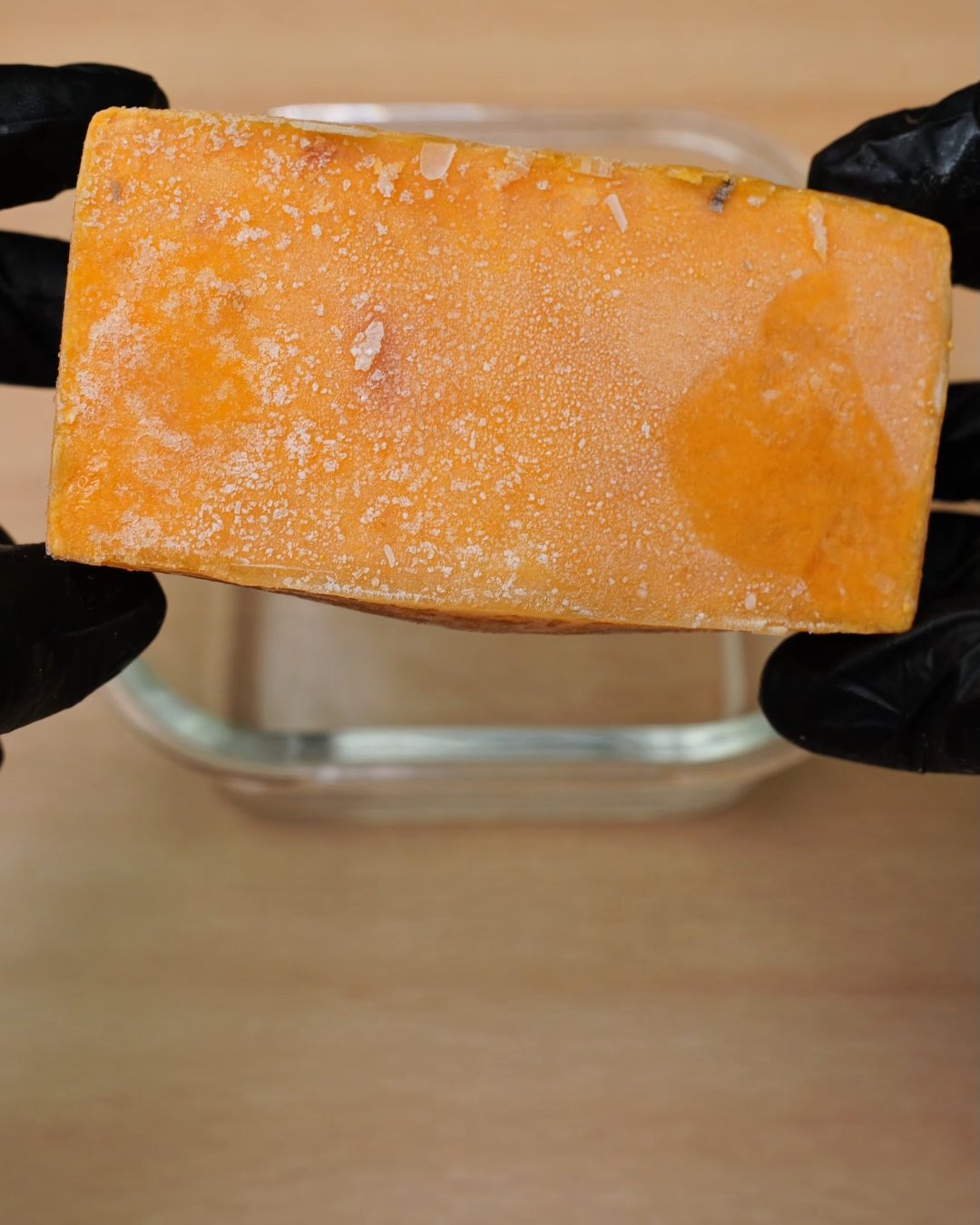 Hands in black gloves holding a frozen tomato cream sauce block over a glass container