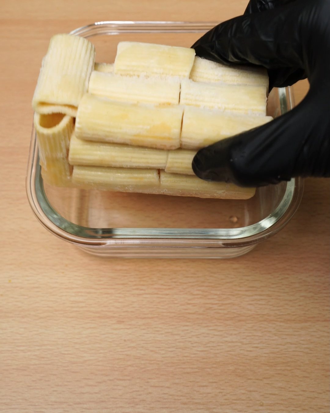 Block of frozen cooked rigatoni being placed into a glass container