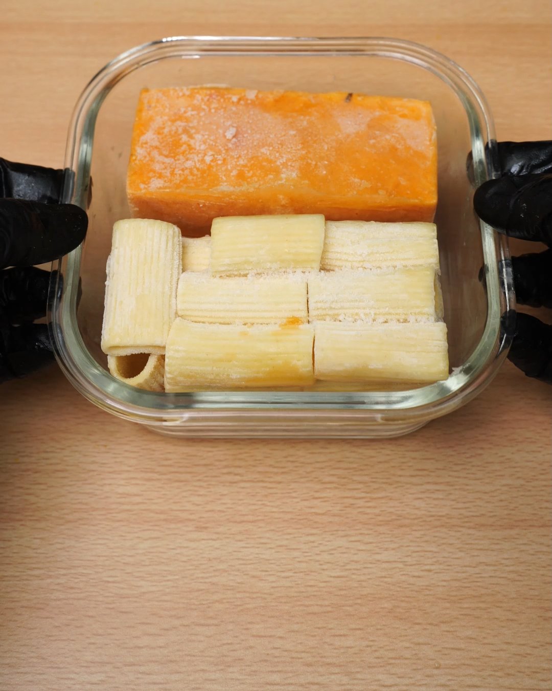 Glass container packed with a frozen tomato cream sauce block and frozen rigatoni