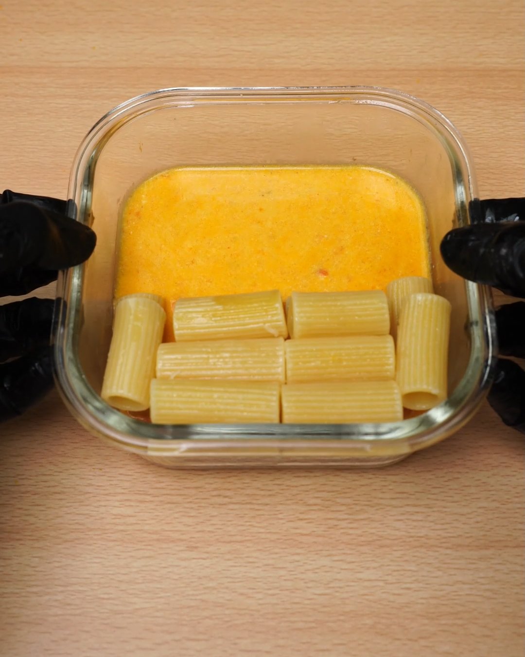 Melted tomato cream sauce beside warm rigatoni in a glass container after microwaving