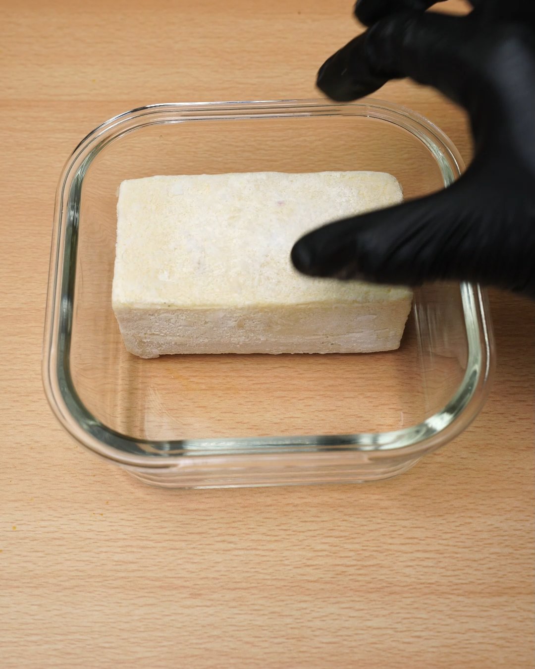 Frozen Alfredo sauce block being set into a square glass container