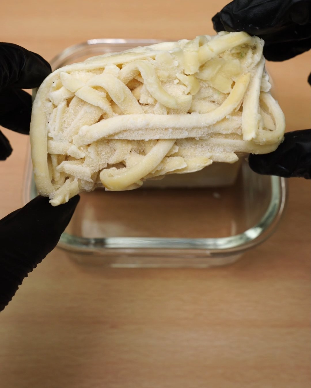 Block of frozen cooked fettuccine being placed into a glass container