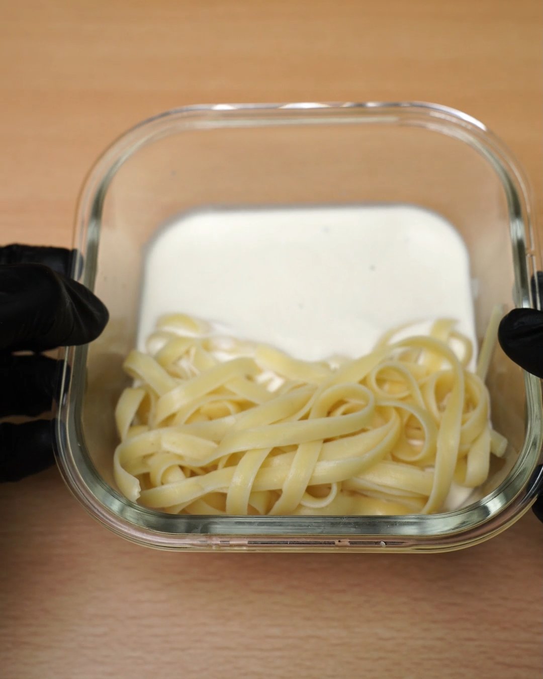 Melted Alfredo sauce beside warm fettuccine in a glass container after microwaving