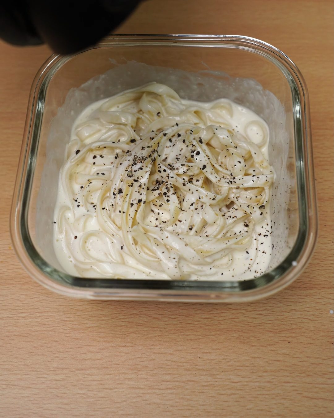 Fettuccine Alfredo sprinkled with cracked black pepper in a glass container