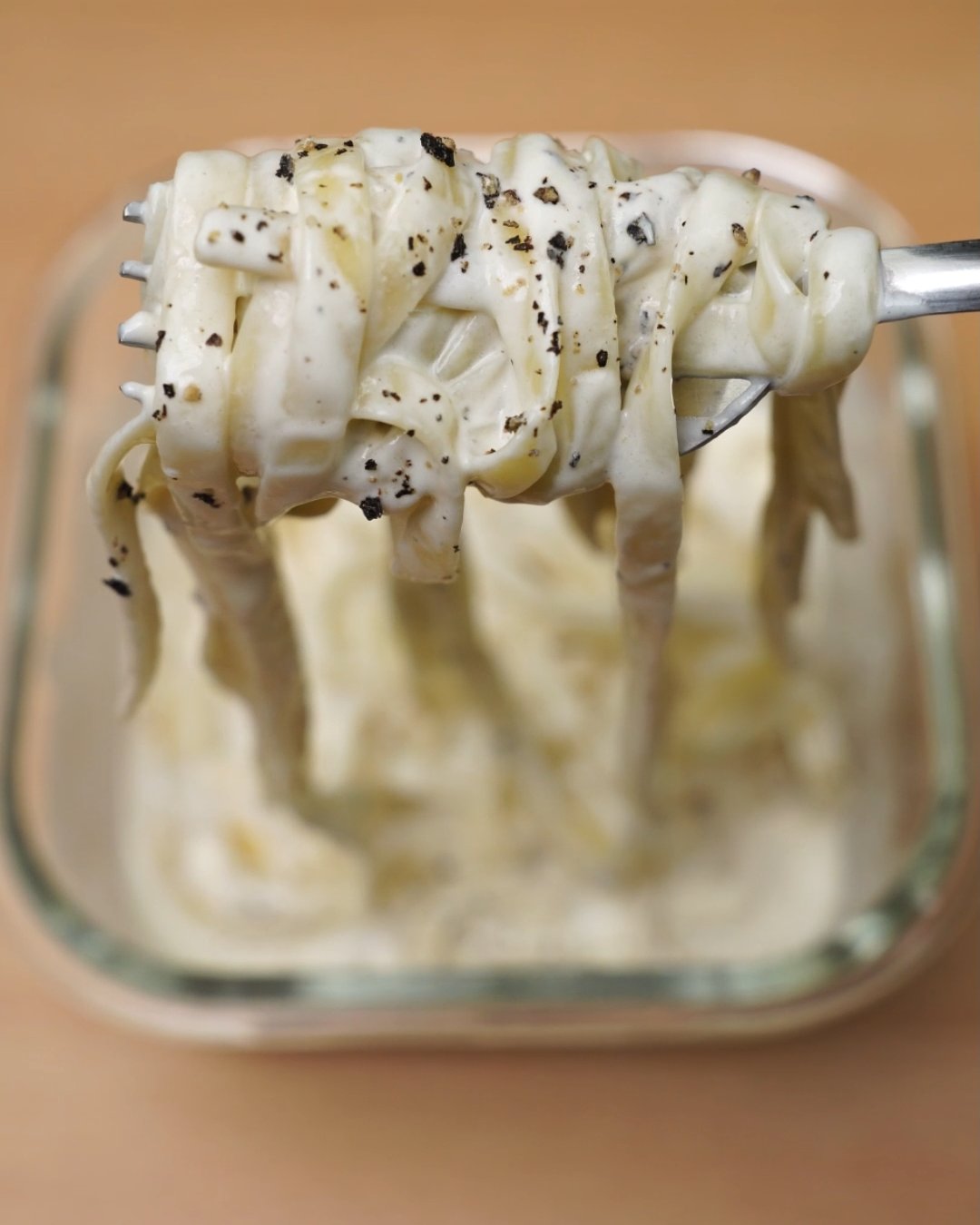 Forkful of creamy fettuccine Alfredo with black pepper lifted from a glass container