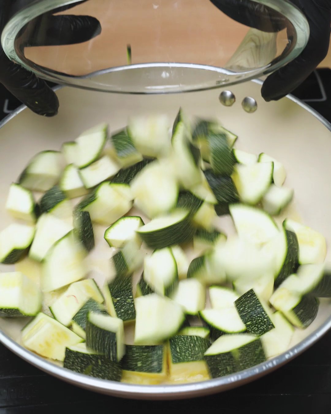 Diced zucchini being added to olive oil in a large skillet