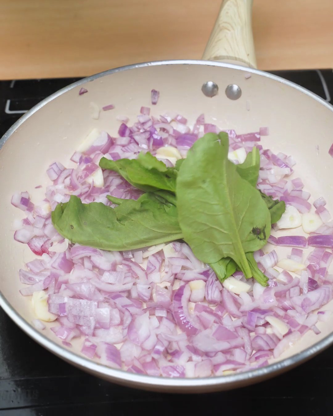 Fresh basil leaves on top of softened red onion and garlic in a skillet