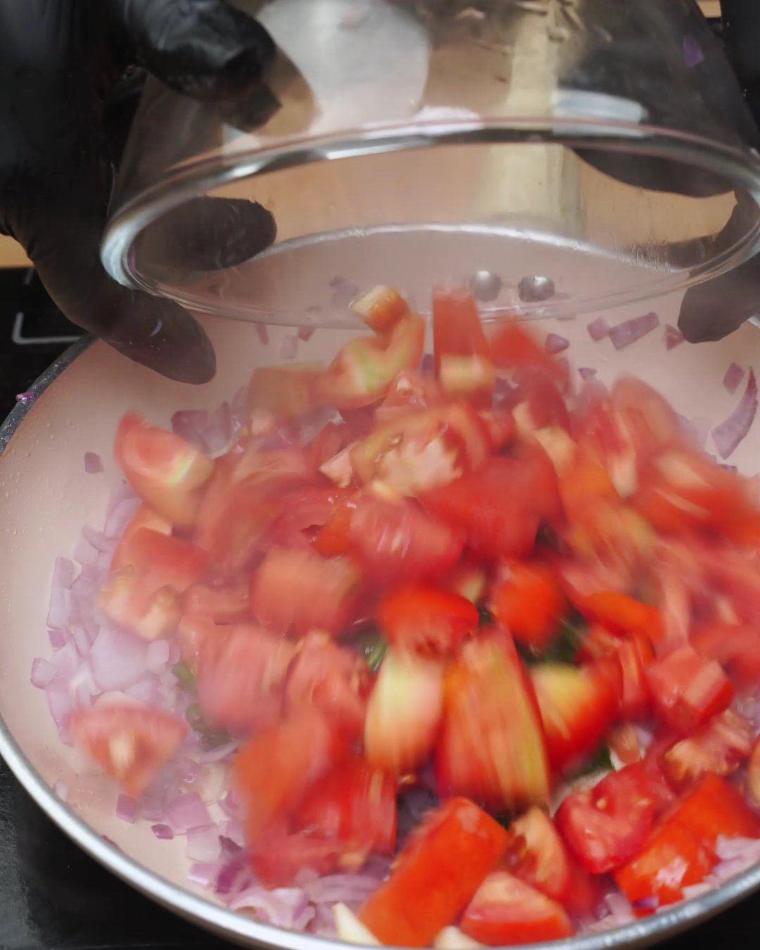 Chopped fresh tomatoes being added to red onion, garlic and basil in a skillet