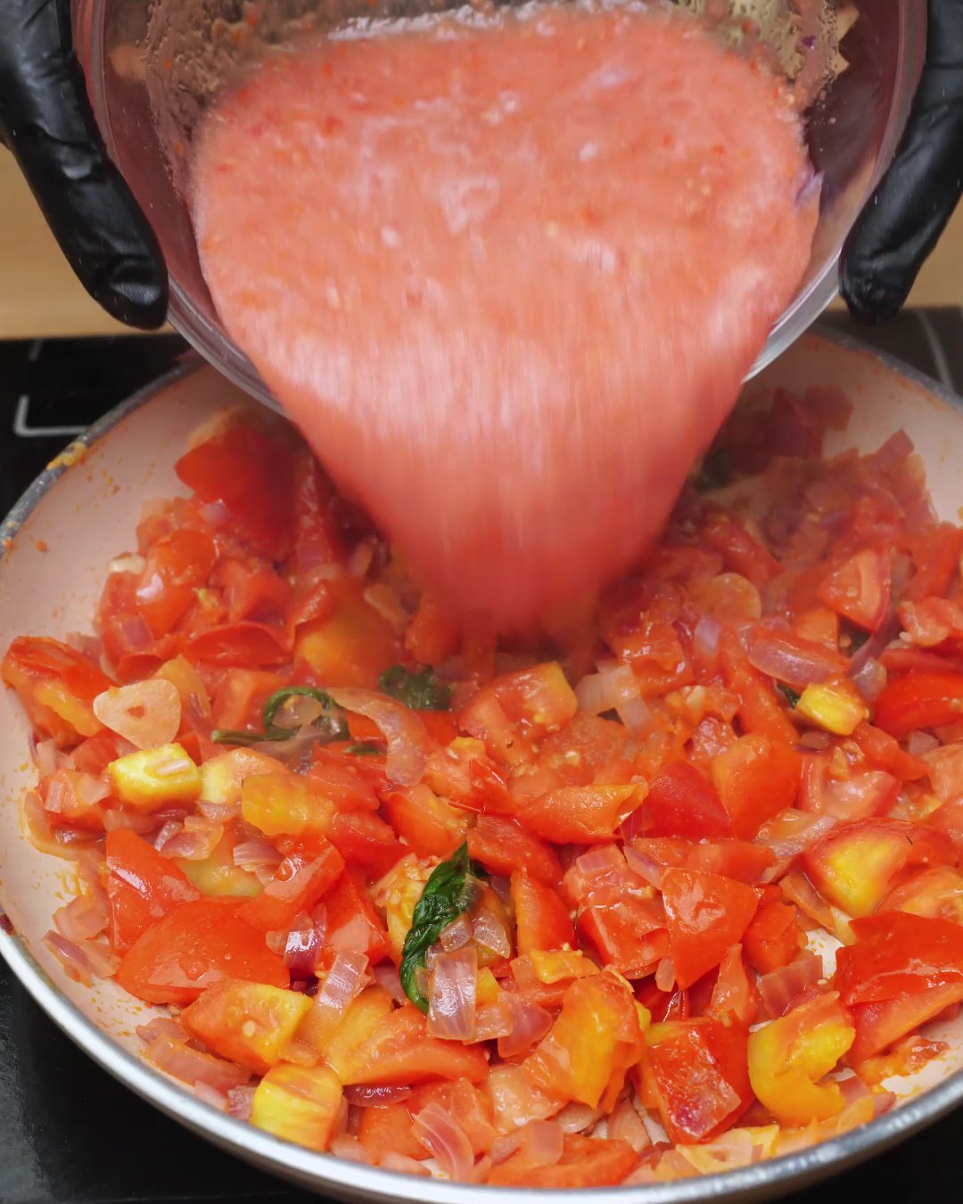 Blended tomatoes being poured over chopped tomatoes and corn in a skillet