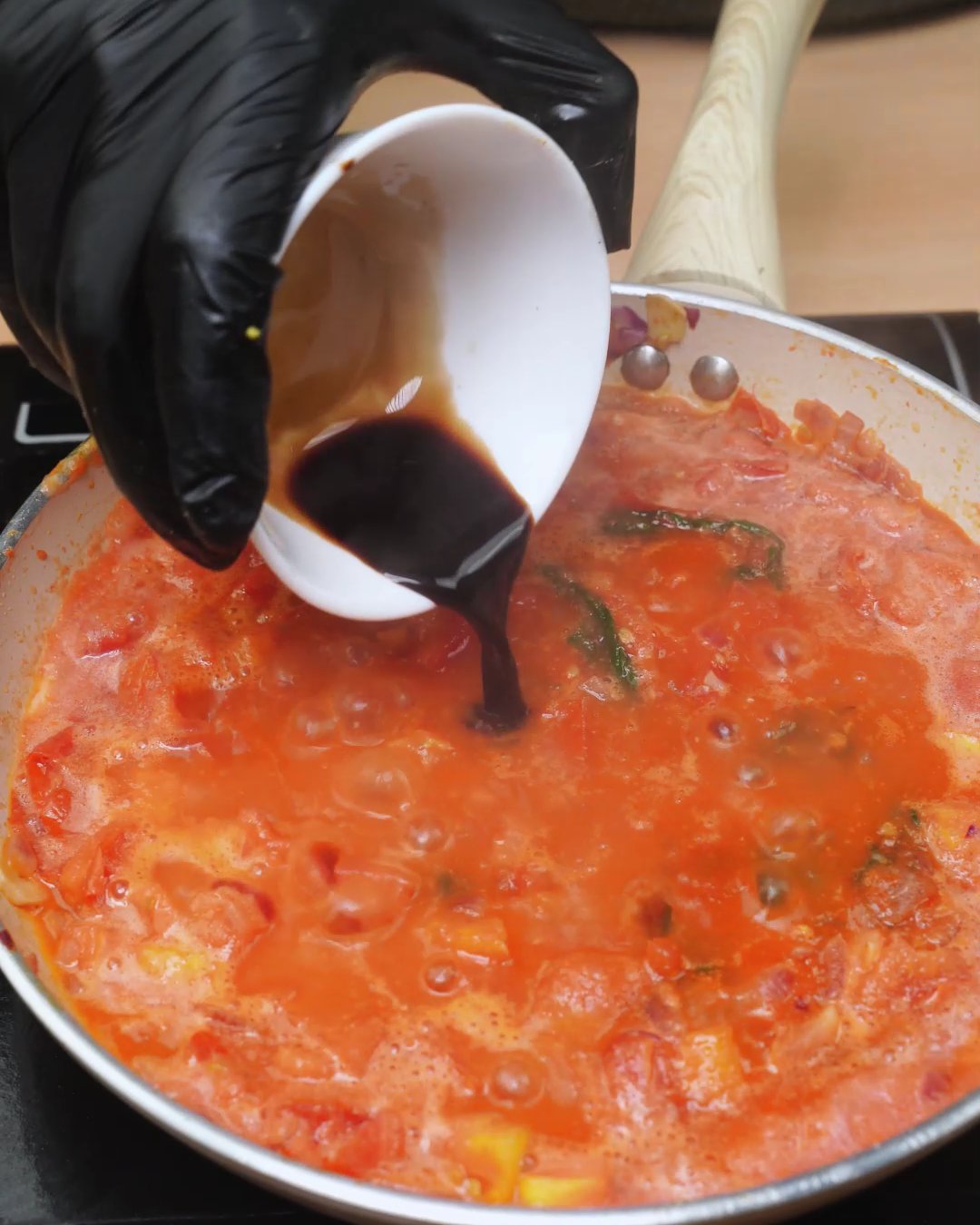 A splash of balsamic vinegar being poured into tomato sauce in a skillet