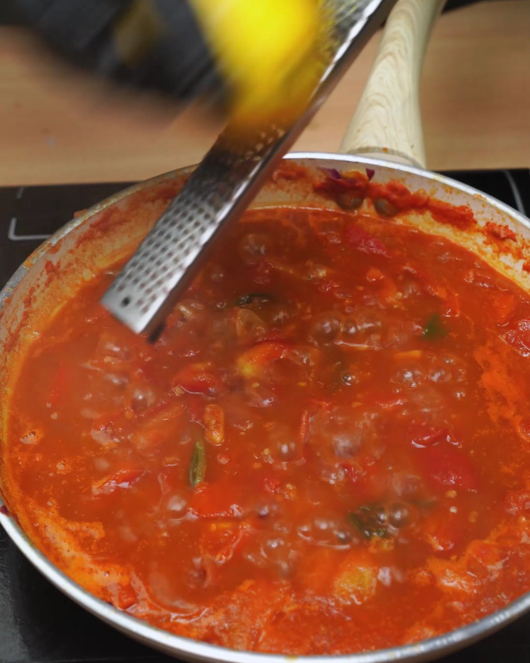 Lemon zest being grated over simmering tomato sauce in a skillet