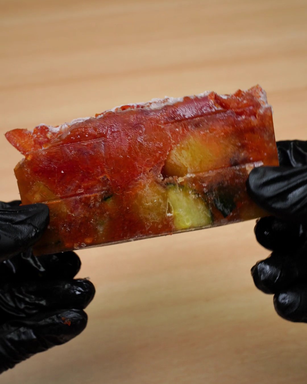 Frozen block of vegetable tomato sauce held in gloved hands